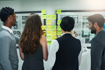 The most successful ideas are formulated as a team. Cropped shot of colleagues brainstorming with adhesive notes on a glass wall in a modern office.