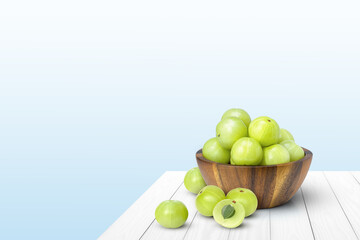 Indian gooseberry fruits or Amla (phyllanthus emblica) in wooden bowl isolated on white wood table with blue background with copy space.