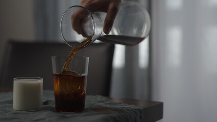 pour cold brewed coffee in tumbler glass with ice ball on wood table