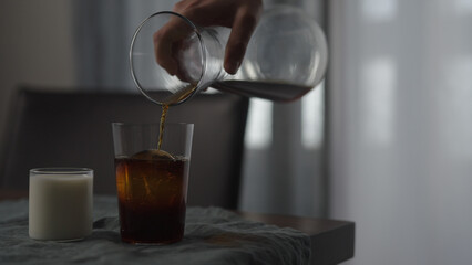 pour cold brewed coffee in tumbler glass with ice ball on wood table
