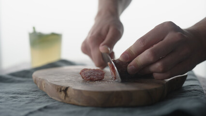 Man slicing mini salami sausage on wood board