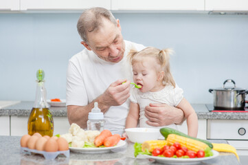 Grandfather feeding baby girl with a spoon at kitchen