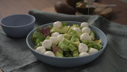 Man making salad with mixed greens avocado and mozzarella in blue bowl