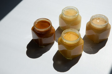 4 types of honey in transparent glass jars on a white background