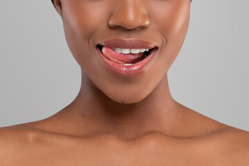 Happy pretty millennial african american woman with perfect smile licks her lips, isolated on gray background