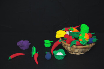 Fototapeta premium Basket of plasticine vegetables and fruits on a black background.