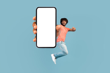 Happy eastern man jumping up and showing cell phone