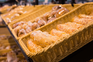 fresh golden breads with melted cheese wrapped in plastic wrap in wicker basket in bread department of supermarket