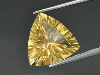 Natural gemstone yellow citrine in tongs on a gray background