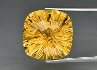 Natural gemstone yellow citrine in tongs on a gray background