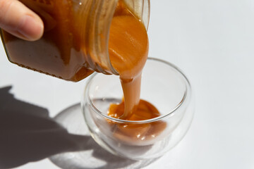 transfusion into a transparent container of brown honey on a white background close up.buckwheat honey