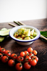 Detail of a bowl of sliced ​​cucumber seasoned with spices and extra virgin olive oil and a bunch of cherry tomatoes.