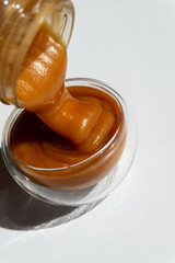 transfusion into a transparent container of brown honey on a white background close up.buckwheat honey