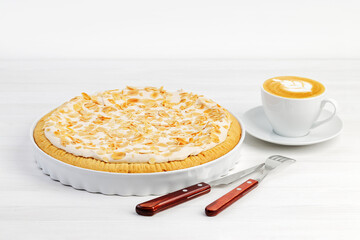 Homemade cake with meringue and almond petals on white wooden table.