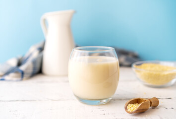 Millet milk in glass, jar and bowl on white wooden table with blue background