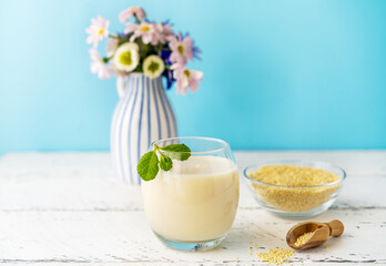 Millet milk in glass and bowl on white wooden table with blue background, mint leaf and vase with...