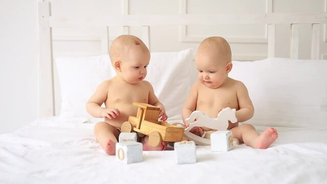 two twin babies in diapers play with wooden toys at home on a bed in a bright white room, children's development