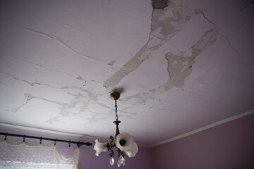 Peeling paint wall of water leak in plaster ceiling. Big wet spots and large crack spots on the...