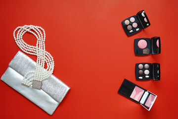Fashion woman bag with makeup cosmetics products and beauty accessories top view on red background copy space, women concept.