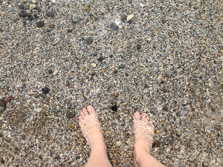 beautiful feet of white woman standing in sea with small pebbles in summer