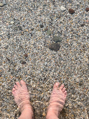  beautiful feet of white woman standing in sea with small pebbles in summer