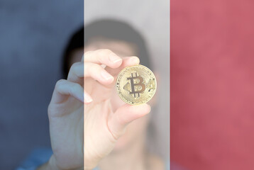 Bitcoin in a woman's hand close-up against the background of the flag of France. Cryptocurrency in France