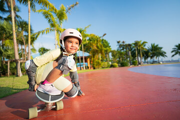 asian child or kid girl playing skateboard or surf skate in skating track and extreme sports exercise by crouching to turn hand touch floor to wearing helmet elbow knee support for body safety protect © kornnphoto