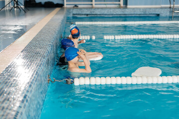 A group of boys and girls train and learn to swim in a modern swimming pool with an instructor. Development of children's sports. Healthy parenting and promotion of children's sports.