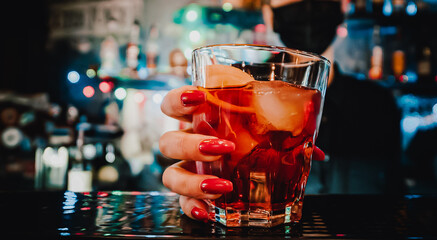 bartender woman hand hold negroni cocktail on bar.