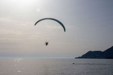 Paragliding with sunset reverse light, parachute silhouette , background mountain and sea