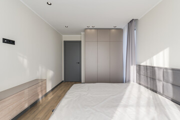 Empty room in a modern style with a large bed, light walls and a stylish gray wardrobe
