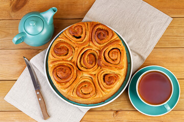 Homemade cinnamon rolls from yeast dough and cup of tea on wooden table. Top view.