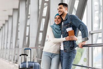 Portrait Of Cheerful Islamic Couple Waiting For Flight At Airport Terminal