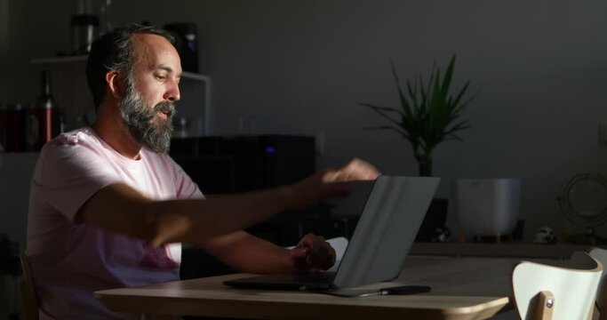 middle-aged bearded man receiving bad news while using his laptop sitting at a table