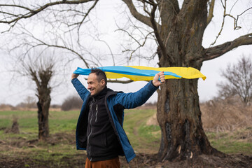 Ukrainian man. Young smiling man holding ukrainian flag. No war. Support for Ukraine. Patriotic Spirit rising hand of Ukraine flag. freedom ukraine. Nature background