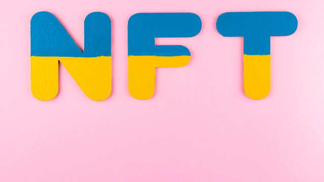 NFT Non-Fungible Token in Ukrainian flag colors. Blue-yellow NFT inscription on pink background. Ukraine support concept. Top view. Copy space