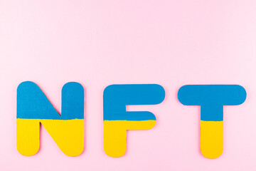 NFT Non-Fungible Token in Ukrainian flag colors. Blue-yellow NFT inscription on pink background. Ukraine support concept. Top view. Copy space