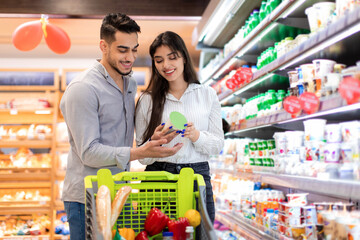 Middle Eastern Couple On Grocery Shopping Holding Jar In Supermarket