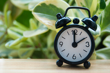 Black alarm clock isolated on blurred nature background. The clock set at 2 o'clock. Copy space concept