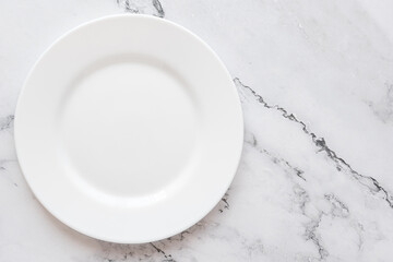 A plate against the background of a marble and concrete countertop. View from above. Small flat round white plate. Place for text.