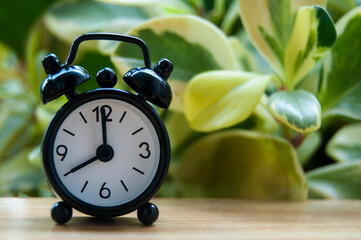Black alarm clock isolated on blurred nature background. The clock set at 8 o'clock.