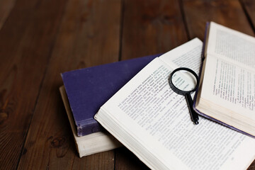 Stack of antique books with magnifying glass on wooden table