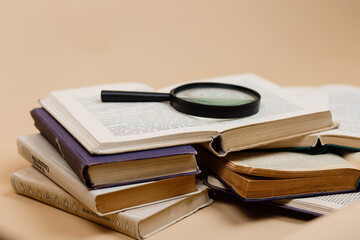 World book daу. A stack of books with a magnifying glass highlighted on a beige background. Search for information.
