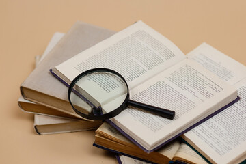World Book Day. A stack of books with a magnifying glass highlighted on a beige background. Search for information.