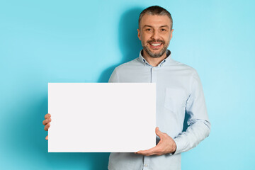 Cheerful Middle Aged Male Holding Blank Paper Poster, Blue Background