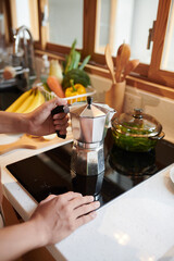 Hands of man putting moka pot on stove when making morning coffee