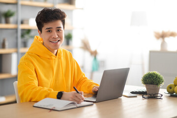 Smiling asian man working on laptop and writing