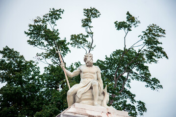 statue of ancient god Neptune with trident on tree background with green leaves. Patron of horses and chariot races. A god of moisture, of the sea, and a protector of drought. © anko_ter