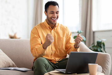Excited man using laptop celebrating success shaking fists
