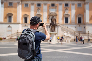 Man tourist sightseeing Rome landmarks and taking photo by smartphone. Europe, Italy trip on summer vacation